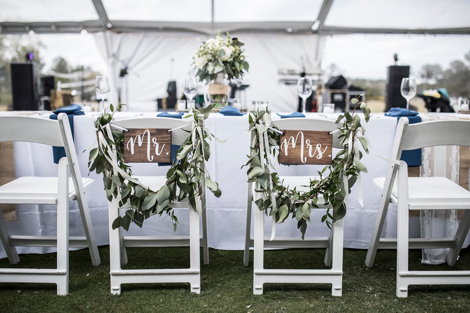 Chairs marked his and hers at a table in a tent at a wedding reception
